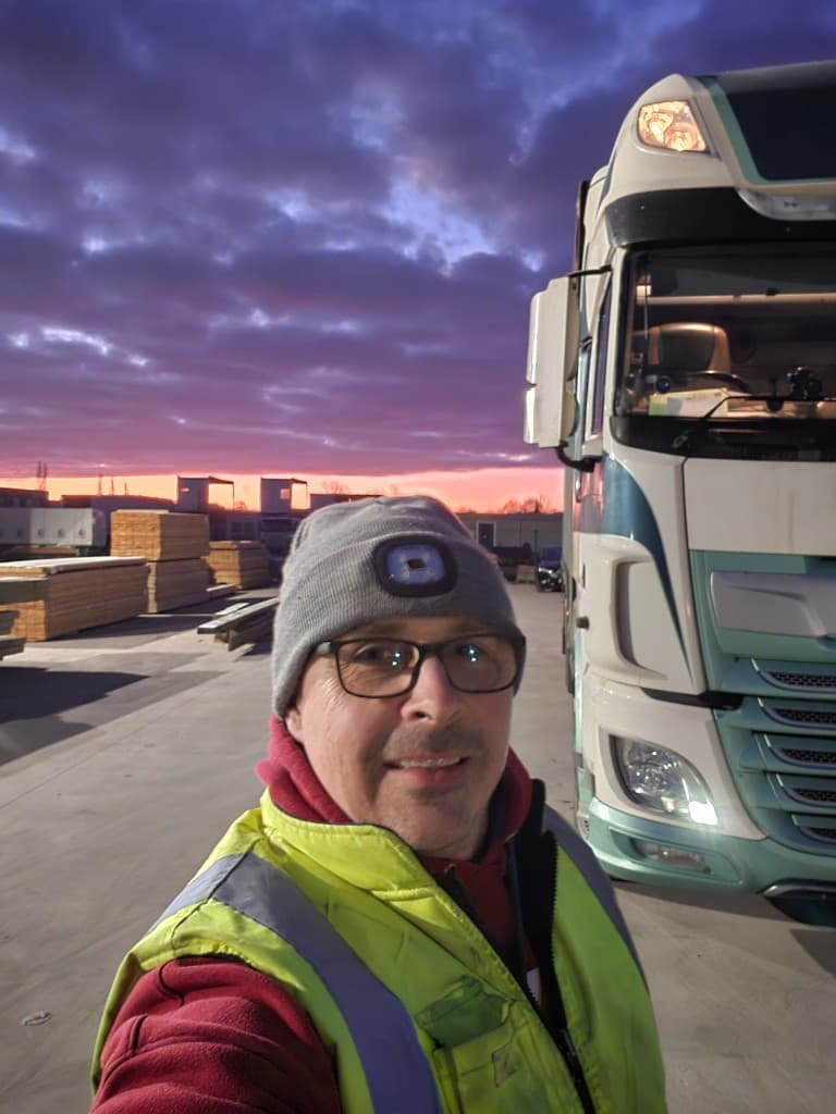 Shane Fullwood in hi-vis workwear at a timber yard at dusk, beside a delivery lorry
